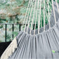 Gray hanging hammock chair with pillows featuring sturdy ropes and fringe detail in outdoor setting