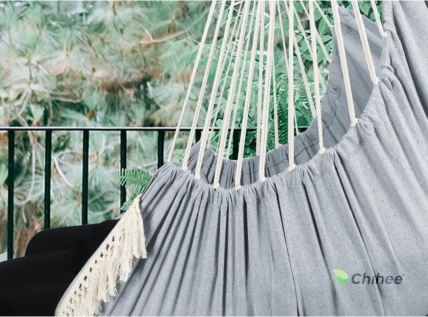 Gray hanging hammock chair with pillows featuring sturdy ropes and fringe detail in outdoor setting