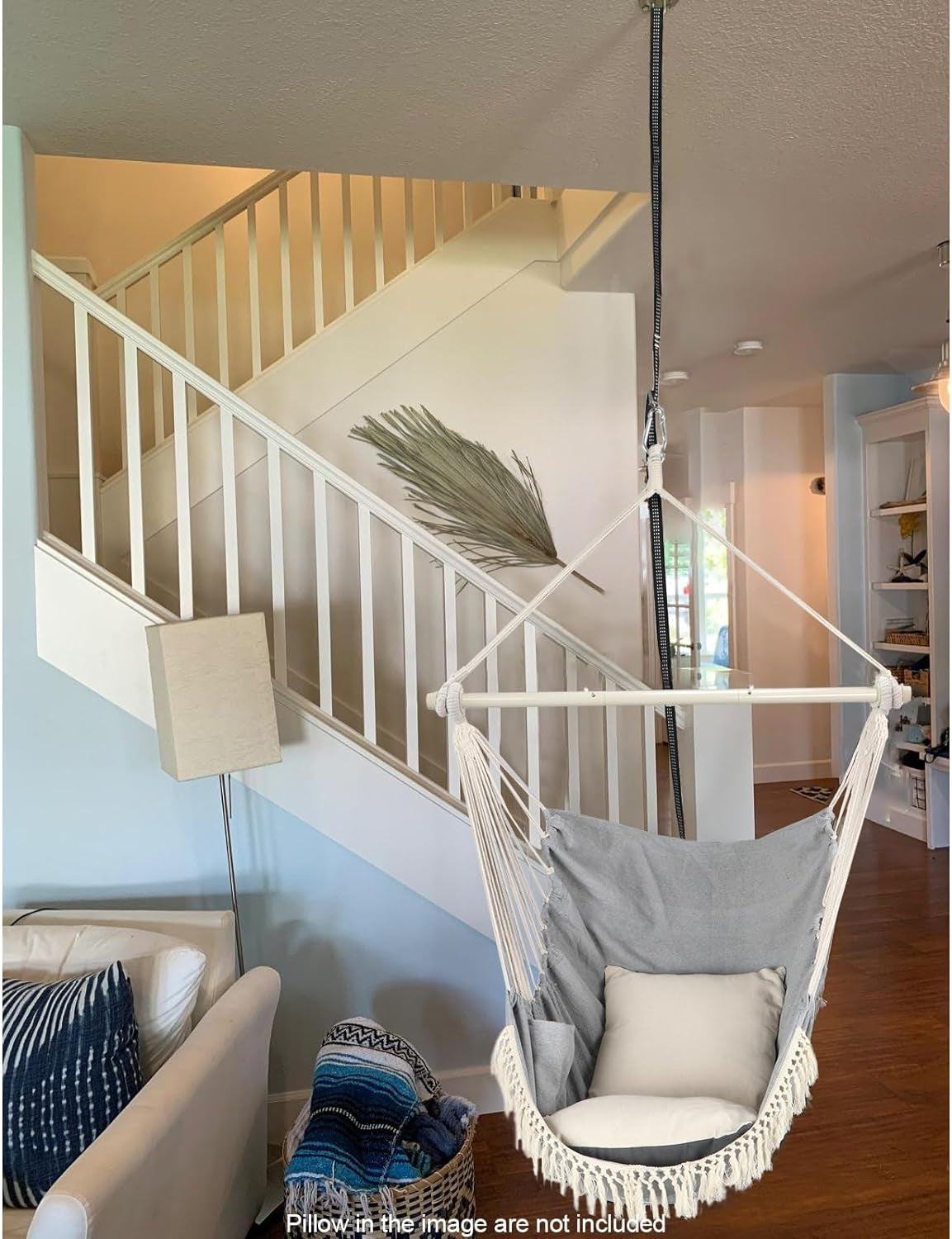 Cozy hanging hammock chair with pillows suspended indoors near staircase in a modern living room